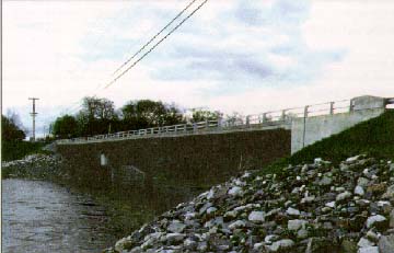 photo: bridge with metal railings spanning a river with rocky banks