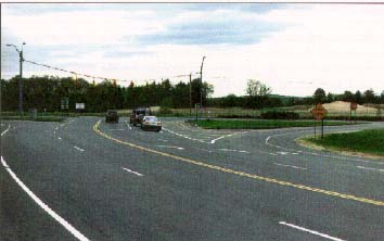 photo: four lane road with a T intersection and two traffic islands