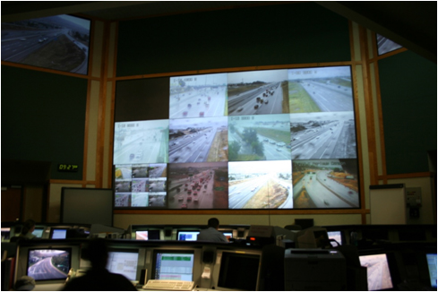 Figure 4.2 - Photo - This figure shows a picture of the control room at the Utah DOT Traffic Operations Center. Active operator workstations are shown in the picture along with the large screens in front of the room that have pictures from the roadway cameras.