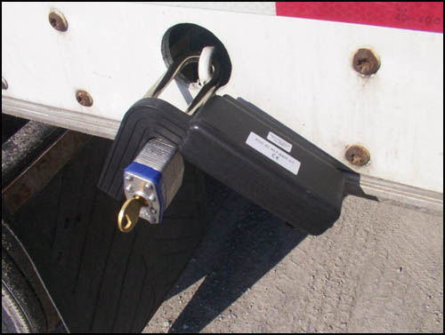 Picture of the Electronic Seal attached to the exterior of the trailer door. In this test, a typical padlock is used on the trailer door hasp and the seal is locked to the pad lock. If deployed, the electronic seal would take the place of the padlock.