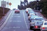 Metered on-ramp with two lanes.  The left lane is designed for HOV vehicles and the right lane is a general all purpose lane.  Several vehicles are queued at the meter and must wait to proceed, while one vehicle is shown using the HOV lane, and can freely enter the freeway.  
