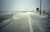 Photograph -Snow covered freeway ramp with a swing-type gate.  The gate is in the closed position, and is posted on the right side of the ramp.