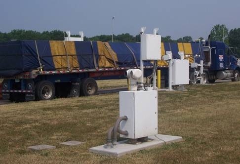 Figure 1. Photograph. Flat-bed semi passing through the ISSES portal, with thermal imaging camera pedestal in foreground (Laurel County, KY).